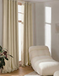 Rideaux sur mesure beige Kurtens à œillets dans salon lumineux avec fauteuil lounge bouclette crème et plante verte