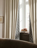 Rideaux sur mesure blanc cassé Kurtens avec doublure matelassée apparente dans salon cosy avec canapé cuir brun et meuble en cannage
