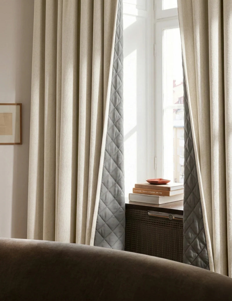 Rideaux sur mesure blanc cassé Kurtens avec doublure matelassée apparente dans salon cosy avec canapé cuir brun et meuble en cannage
