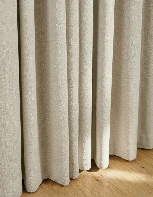 Détail du tombé du rideau sur mesure beige Kurtens en tissu texture naturelle sur parquet en bois clair
