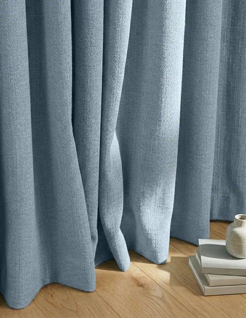 Rideau sur mesure bleu Kurtens, tombé élégant au sol dans un intérieur moderne et lumineux