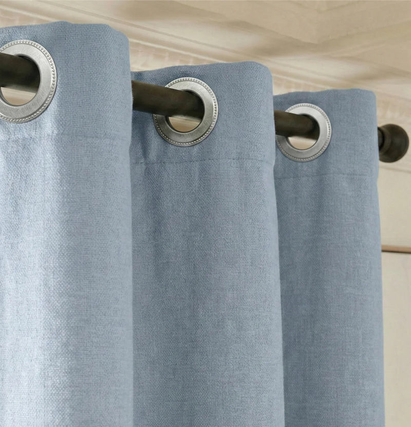 Fixation de rideau sur mesure Kurtens bleu occultant thermique phonique avec œillets métalliques argentés sur tringle noire, gros plan sur le système d'accroche en tissu épais
