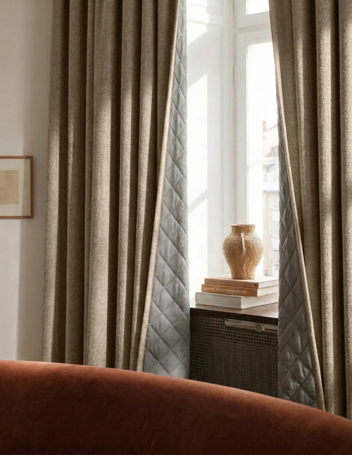 Rideaux sur mesure crème Kurtens installés dans salon chaleureux avec canapé terracotta, vase décoratif et meuble en cannage