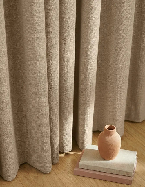 Rideau crème sur mesure Kurtens en tissu texture lin avec tombé lourd, mise en scène vase terre cuite et parquet bois clair