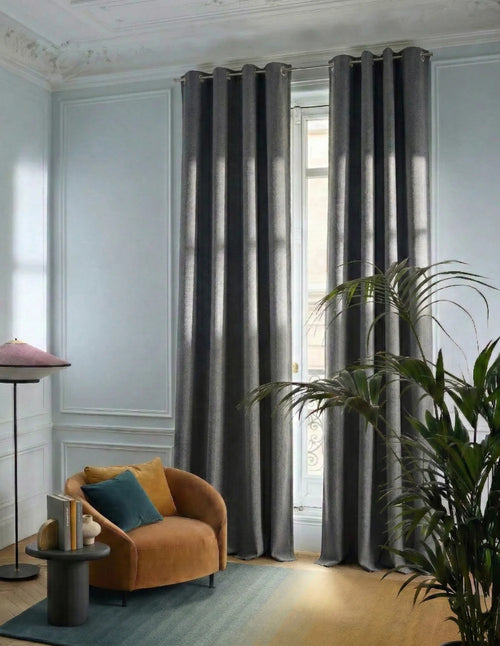 Rideaux sur mesure gris anthracite Kurtens dans salon raffiné avec moulures, fauteuil velours ocre, plante verte et tapis bleu