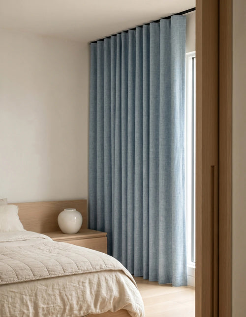 Rideau occultant bleu ciel tiré devant une fenêtre dans une chambre lumineuse en bois clair