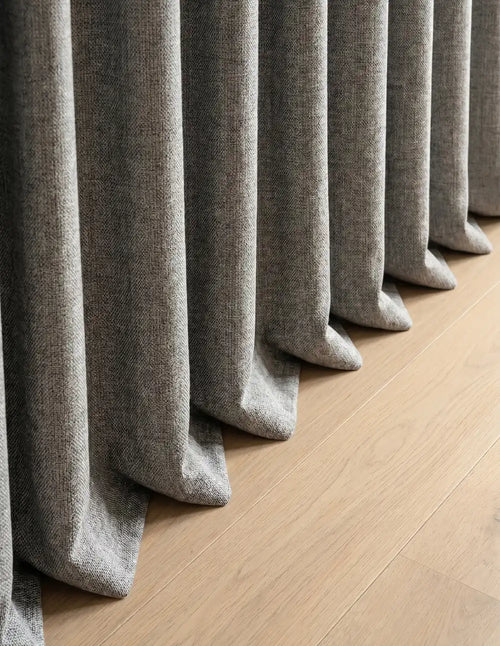 Détail du tombé du rideau occultant gris chiné cassant sur le parquet