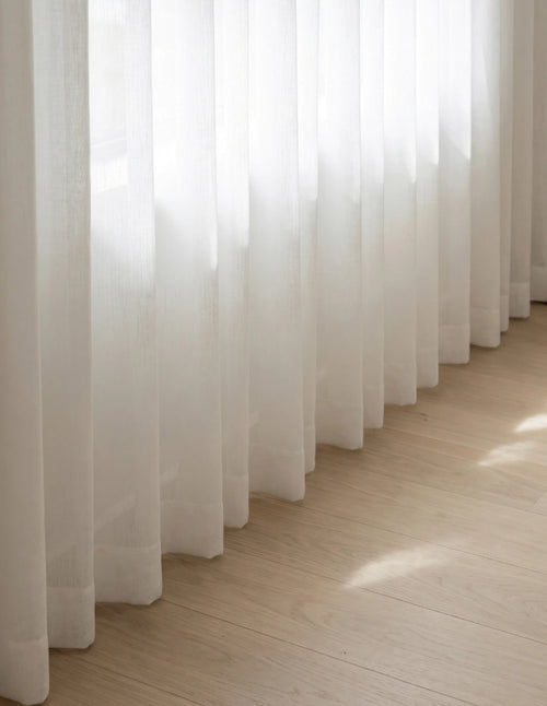 Détail du bas du rideau tamisant blanc effet lin, plis ondulés laissant filtrer la lumière