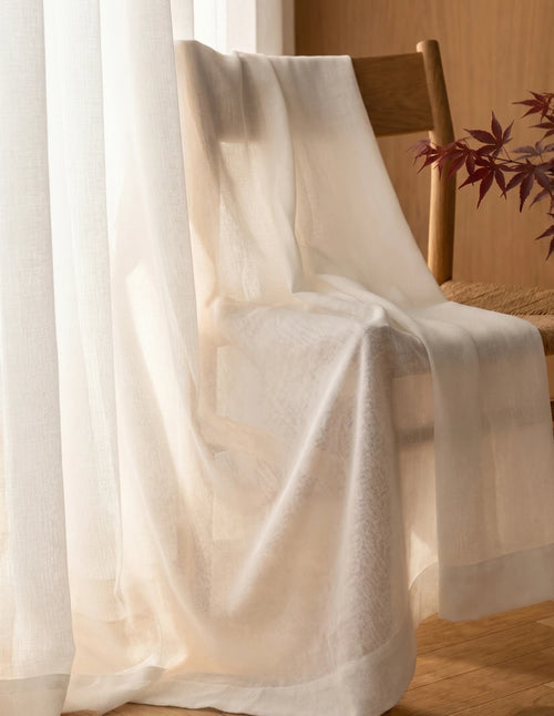 Tissu du rideau tamisant blanc effet lin drapé sur une chaise en bois, lumière du jour traversant la trame
