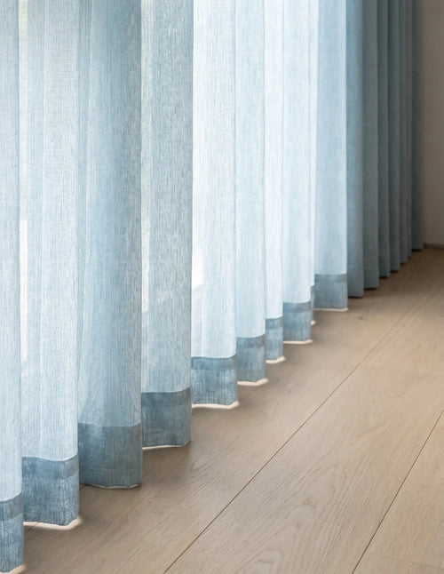 Détail du bas du rideau tamisant bleu effet lin, plis ondulés laissant filtrer la lumière