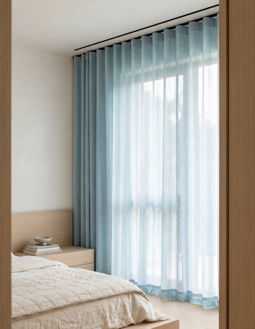 Tissu du rideau tamisant bleu effet lin drapé sur une chaise en bois, lumière du jour traversant la trame