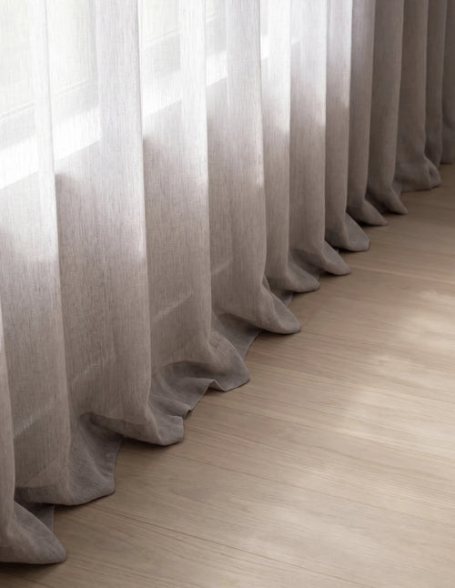 Détail du bas du rideau tamisant gris mauve effet lin, plis ondulés laissant filtrer la lumière