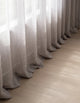 Détail du bas du rideau tamisant gris mauve effet lin, plis ondulés laissant filtrer la lumière