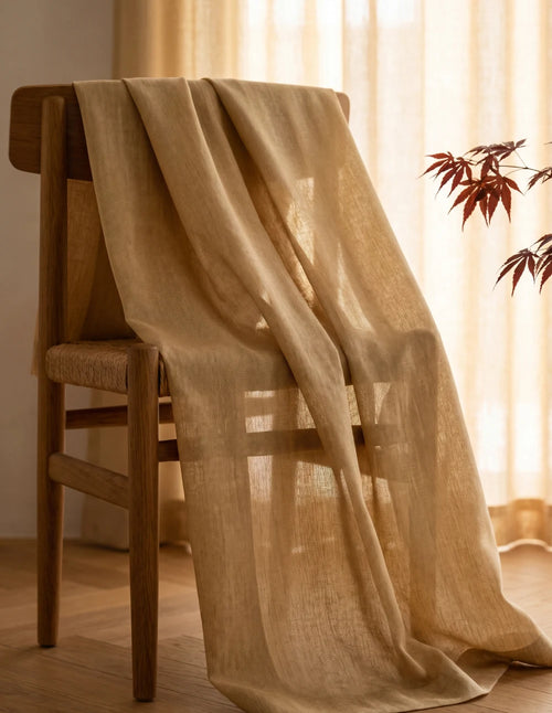 Tissu du rideau tamisant sable effet lin drapé sur une chaise en bois, lumière du jour traversant la trame