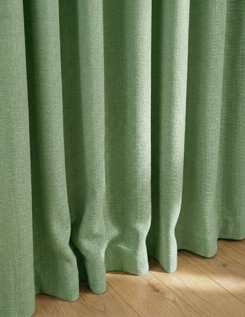 Tombé lourd et naturel du rideau sur mesure vert sauge Kurtens en tissu texture lin sur parquet bois clair