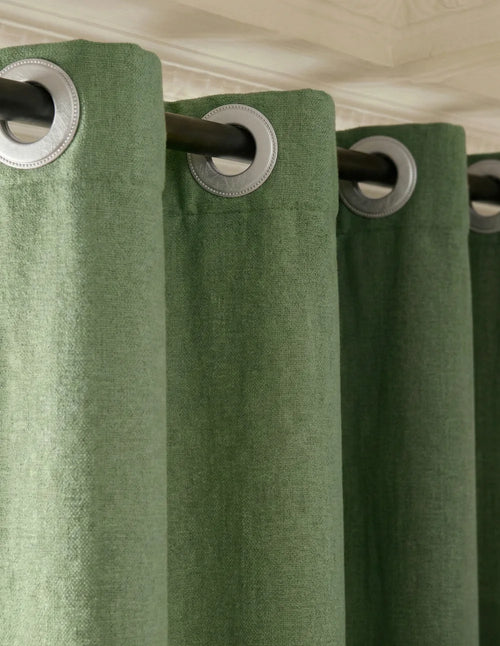 Gros plan du rideau sur mesure vert sauge Kurtens avec œillets métalliques, textile texturisé sous moulures classiques