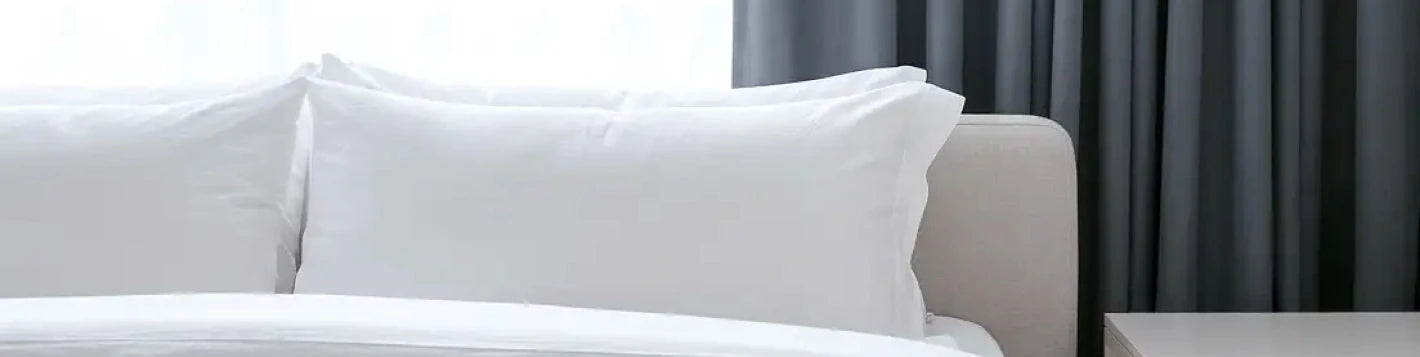 Bannière rideaux sur mesure gris foncé Kurtens dans une chambre premium à linge blanc et tête de lit crème