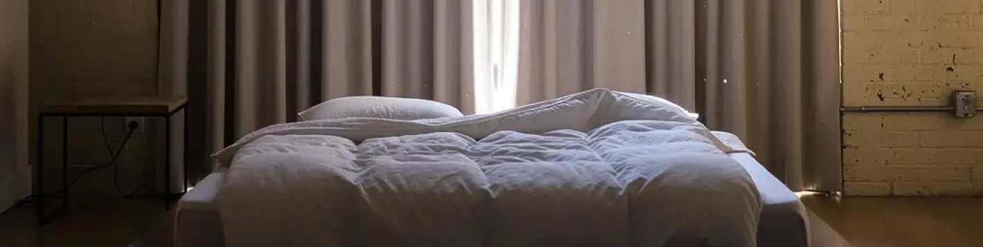 Bannière rideaux sur mesure beige occultants Kurtens dans une chambre loft à mur de briques, lumière tamisée