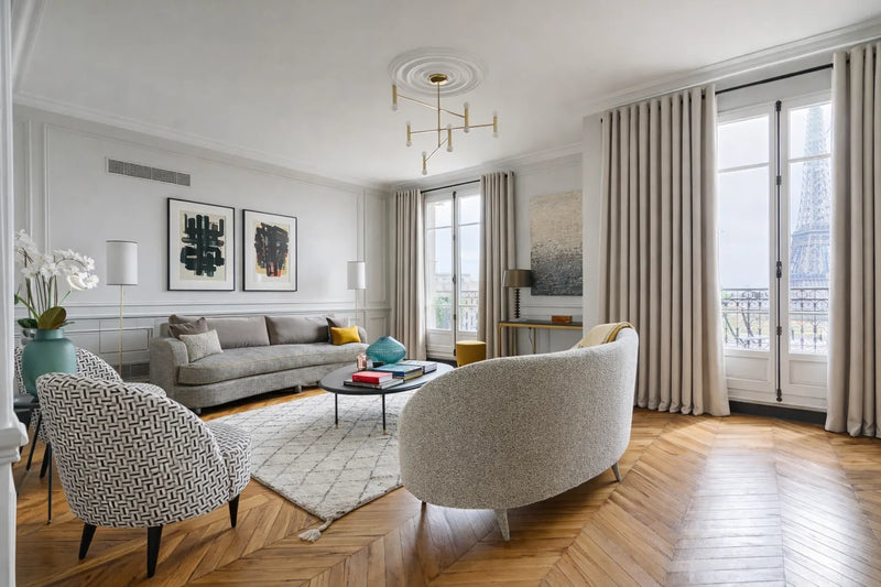 Rideaux sur mesure beige Kurtens dans un salon parisien avec vue sur Tour Eiffel et parquet chevron haussmannien