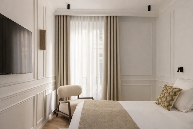 Rideau sur mesure beige avec voilage Kurtens dans une chambre haussmannienne élégante à lit crème